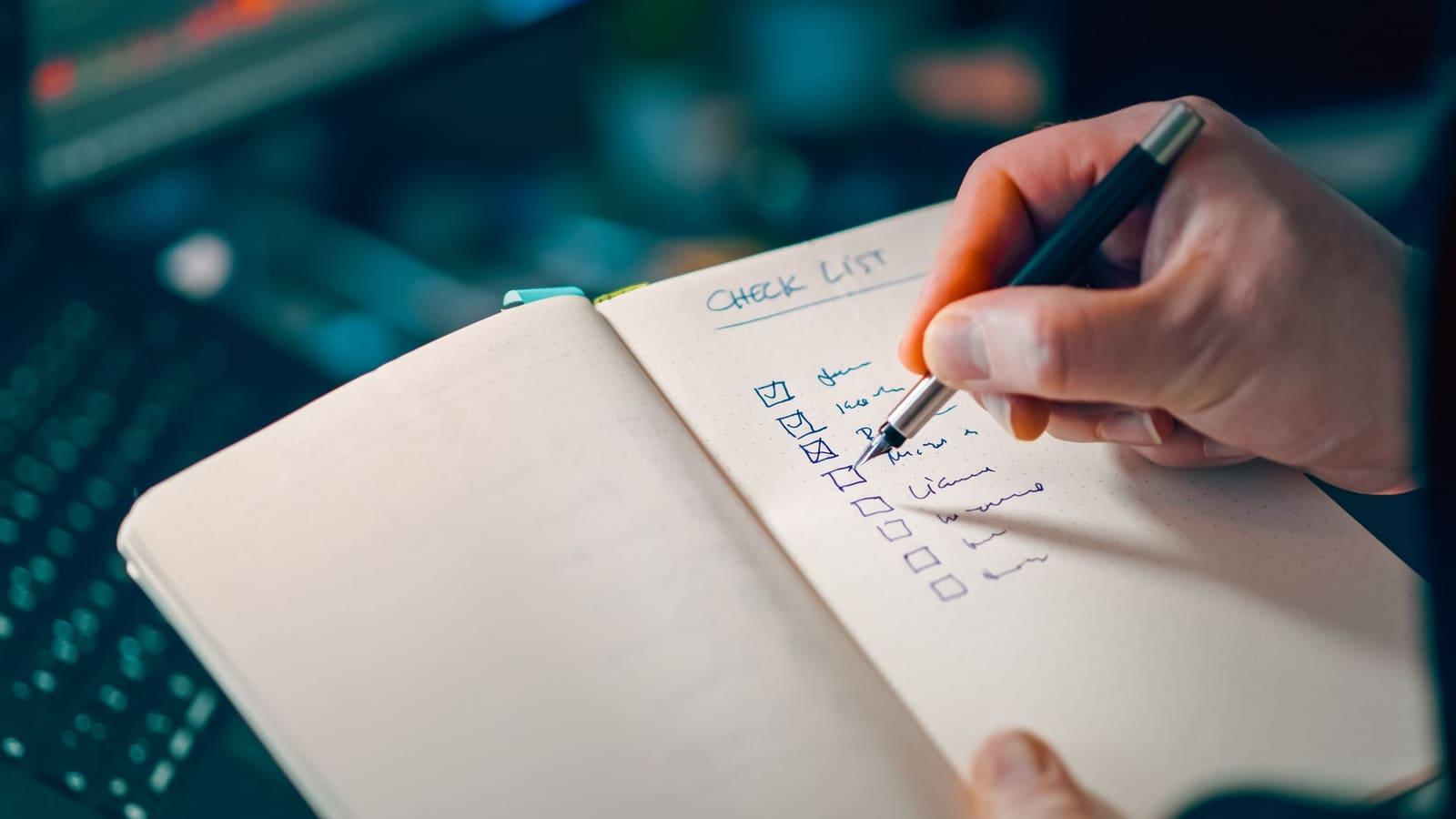 A hand writing in an open notebook under the heading Check List, with several boxes ticked