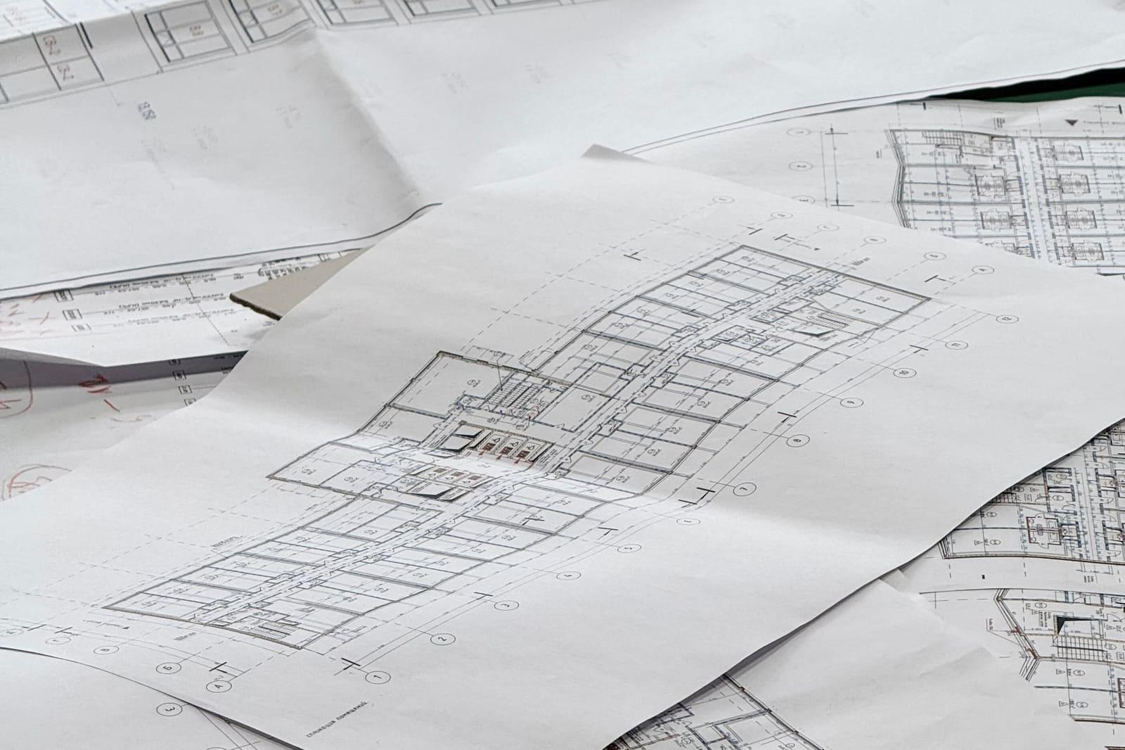 Several large sheets of printed architectural floor plans spread across a table