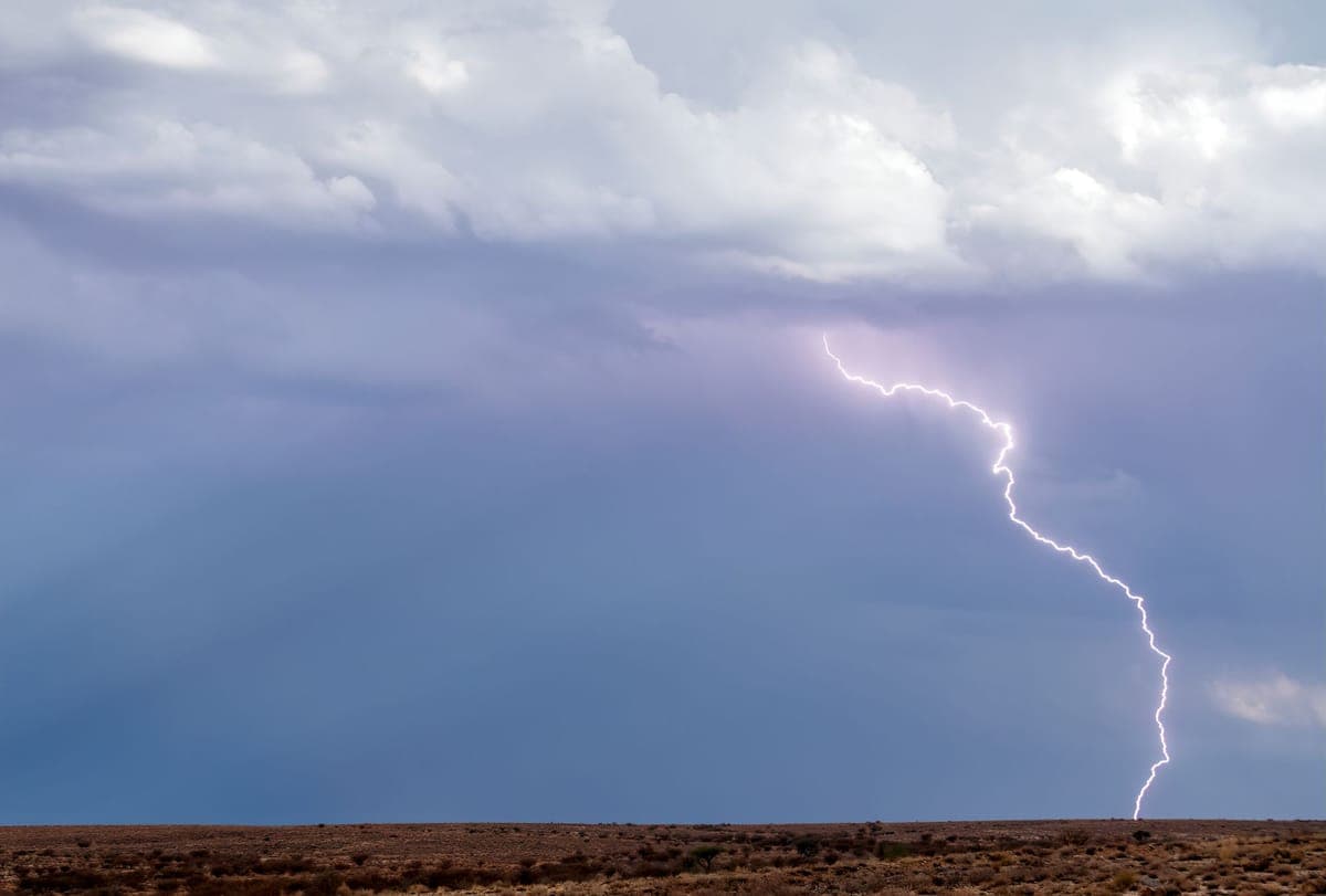 Lightning strikes from dark storm clouds over a flat, dry desert plain