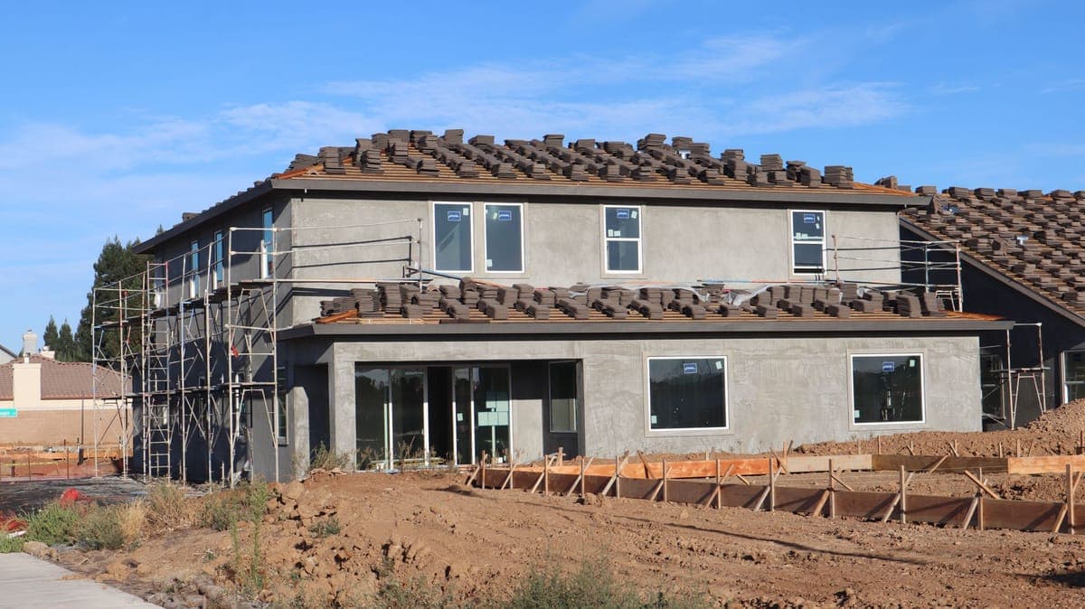New two-story stucco house with stacks of roof tiles set out across the roof