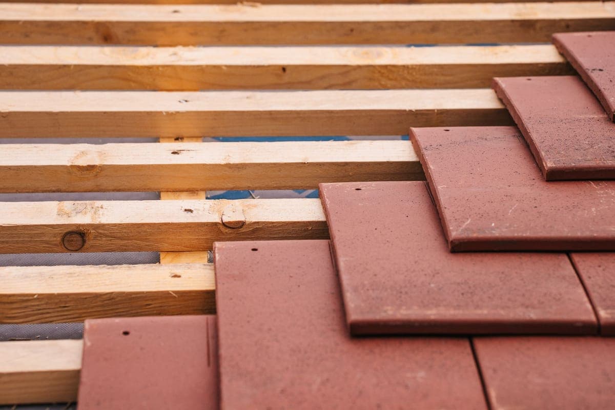 Close-up of red clay roof tiles being laid over wooden battens, with underlayment showing between them